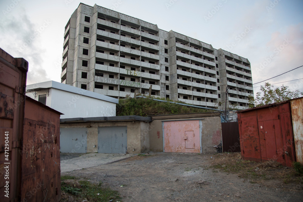 VLADIVOSTOK, RUSSIA. a soviet empty abandoned unfinished haunted residential concrete panel house building with balconies and a writing WE LOVE YOU in Russian and old red garages in front VLADIVOSTOK, RUSSIA. a soviet empty abandoned unfinished haunted residential concrete panel house building with balconies and a writing WE LOVE YOU in Russian and old red garages in front