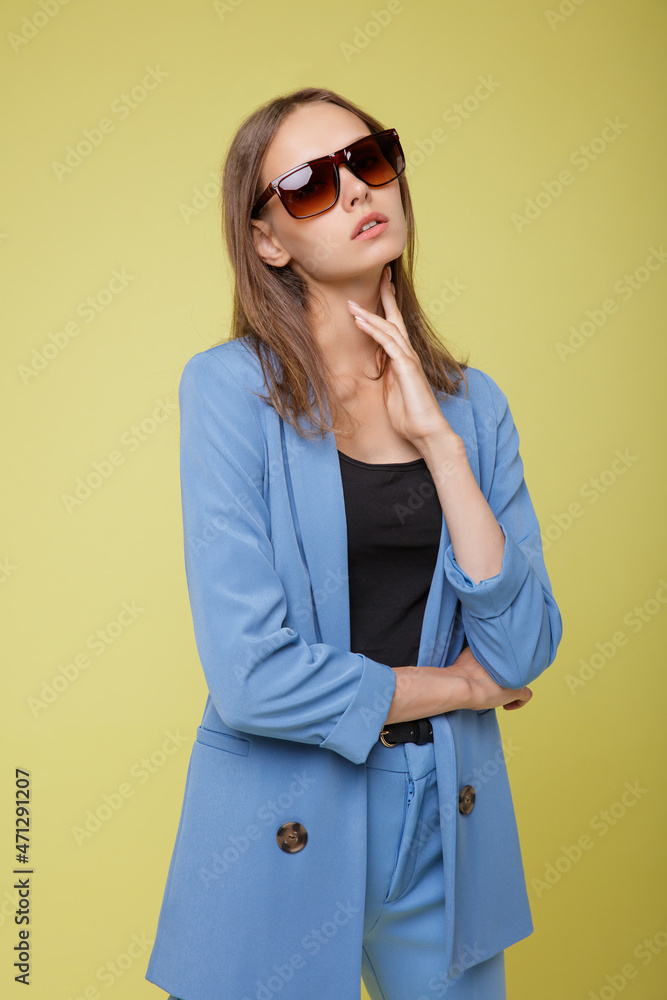 Fashion photo of a beautiful elegant young woman in a pretty blue suit, jacket, pants, trousers stylish sunglasses, trousers posing over yellow lemon background. Studio shot, portrait. Fashion photo of a beautiful elegant young woman in a pretty blue suit, jacket, pants, trousers stylish sunglasses, trousers posing over yellow lemon background. Studio shot, portrait.
