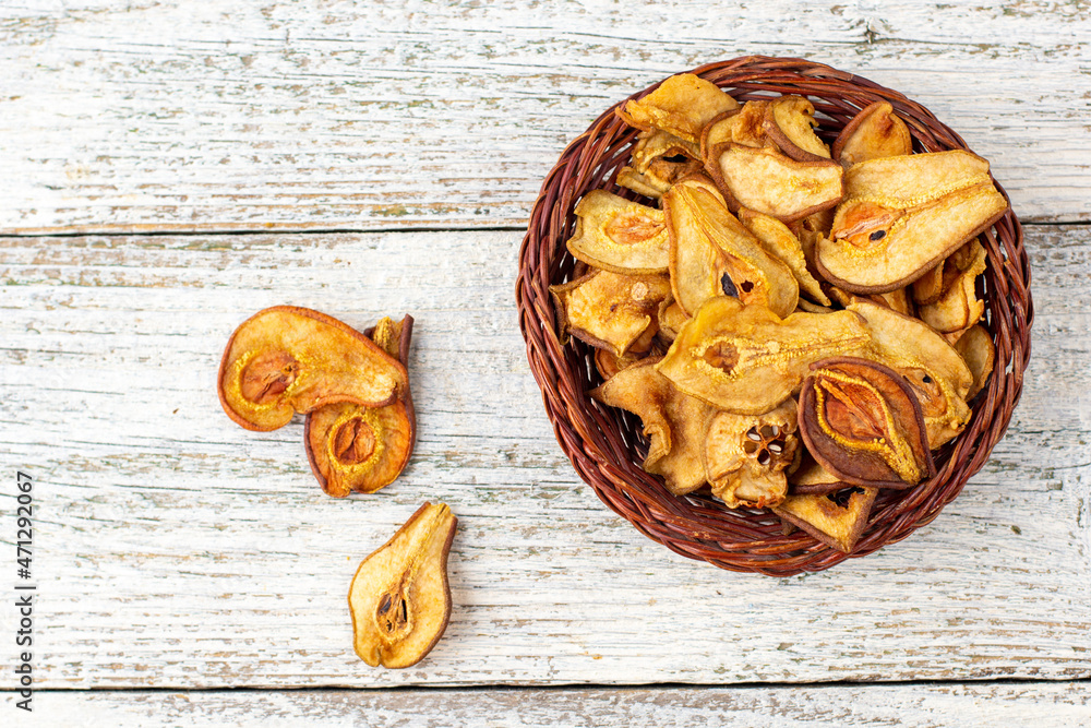 A pile of dried slices of pears in wicker basket on white wooden background. Dried fruit chips. Healthy food