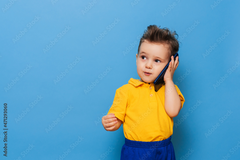 A little boy is talking on a mobile phone. Studio photo on a blue background. A little boy is talking on a mobile phone. Studio photo on a blue background.