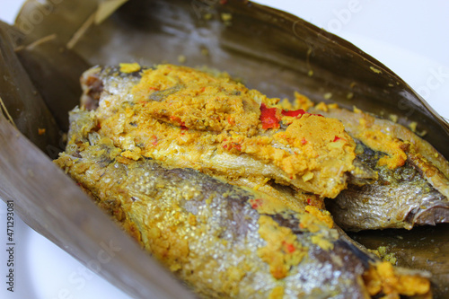 Pepes ikan, or steamed fish with herbs then wrapped in banana leaf. Indonesia traditional food. On a white plate. photo