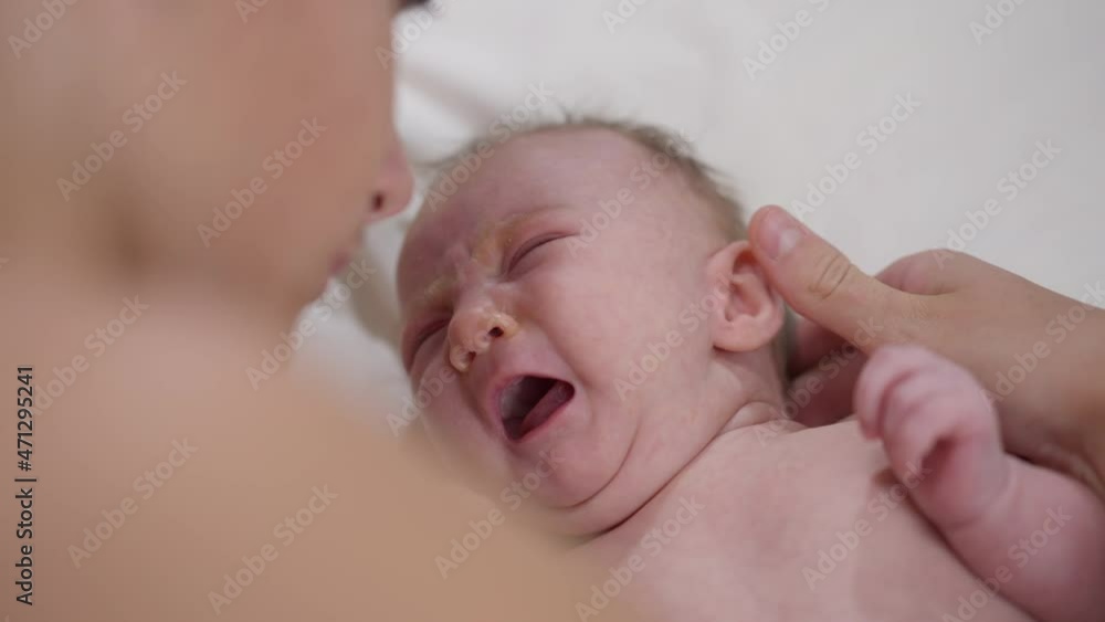 Close-up portrait crying newborn infant with teenage boy stroking ear talking hugging child. Dissatisfied Caucasian baby girl sister with caring loving brother at home indoors Close-up portrait crying newborn infant with teenage boy stroking ear talking hugging child. Dissatisfied Caucasian baby girl sister with caring loving brother at home indoors