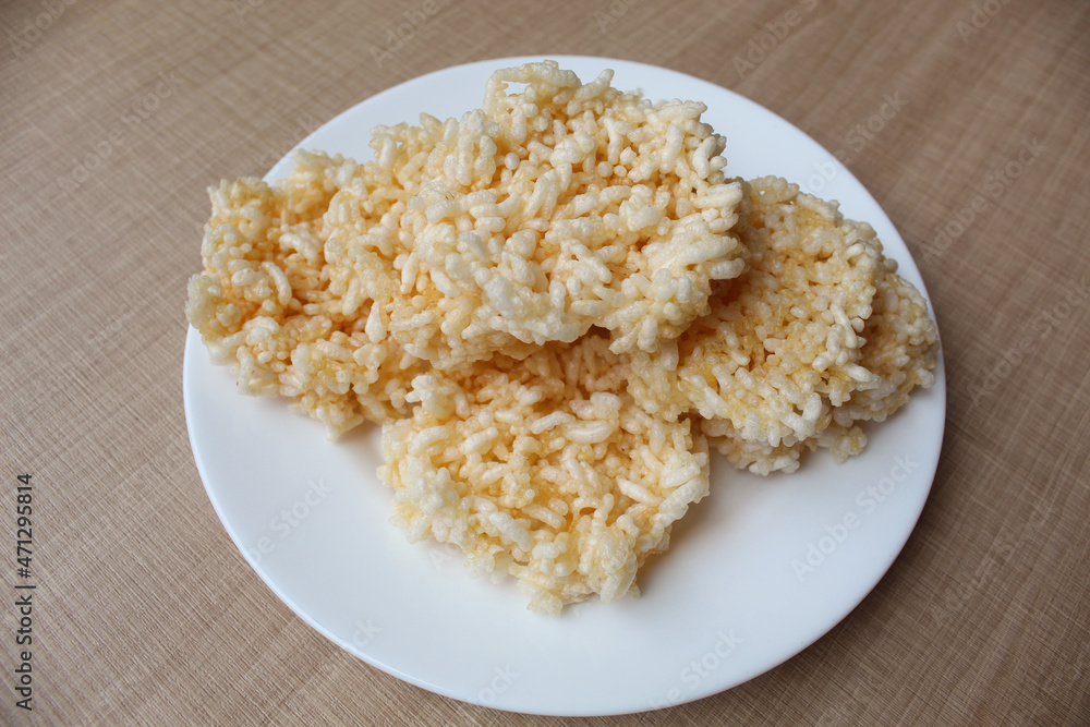 Rengginang, traditional crackers from Indonesia, made from sticky rice which dried then fried. On a white plate. Rengginang, traditional crackers from Indonesia, made from sticky rice which dried then fried. On a white plate.
