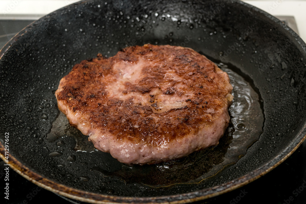 Meat burger being shallow fried in oil on a frying pan, close up, selective focus