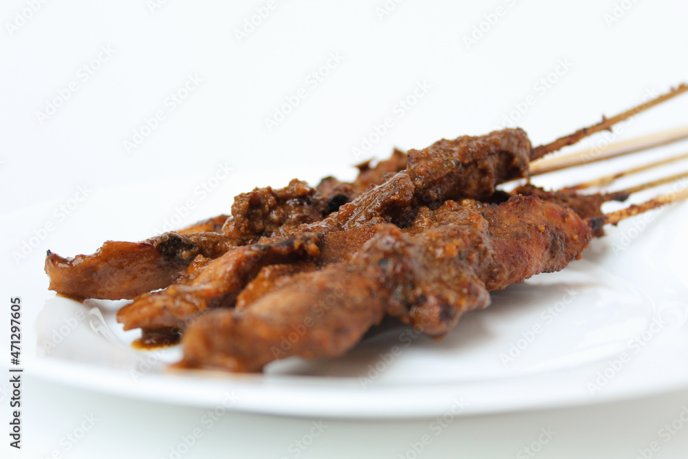 Chicken satay covered by peanut sauce, with bamboo skewers. Indonesian traditional food. On a white plate. Isolated on white background