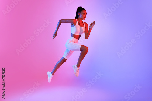 Fitness Lady Jumping Running In Mid-Air Over Neon Background © Prostock-studio