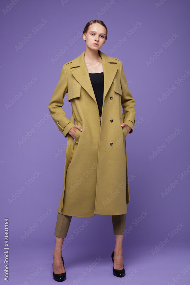 High fashion photo of a beautiful elegant young woman in a pretty yellow mustard coat, pants, trousers posing on a purple lavender background. Studio shot, portrait. High fashion photo of a beautiful elegant young woman in a pretty yellow mustard coat, pants, trousers posing on a purple lavender background. Studio shot, portrait.