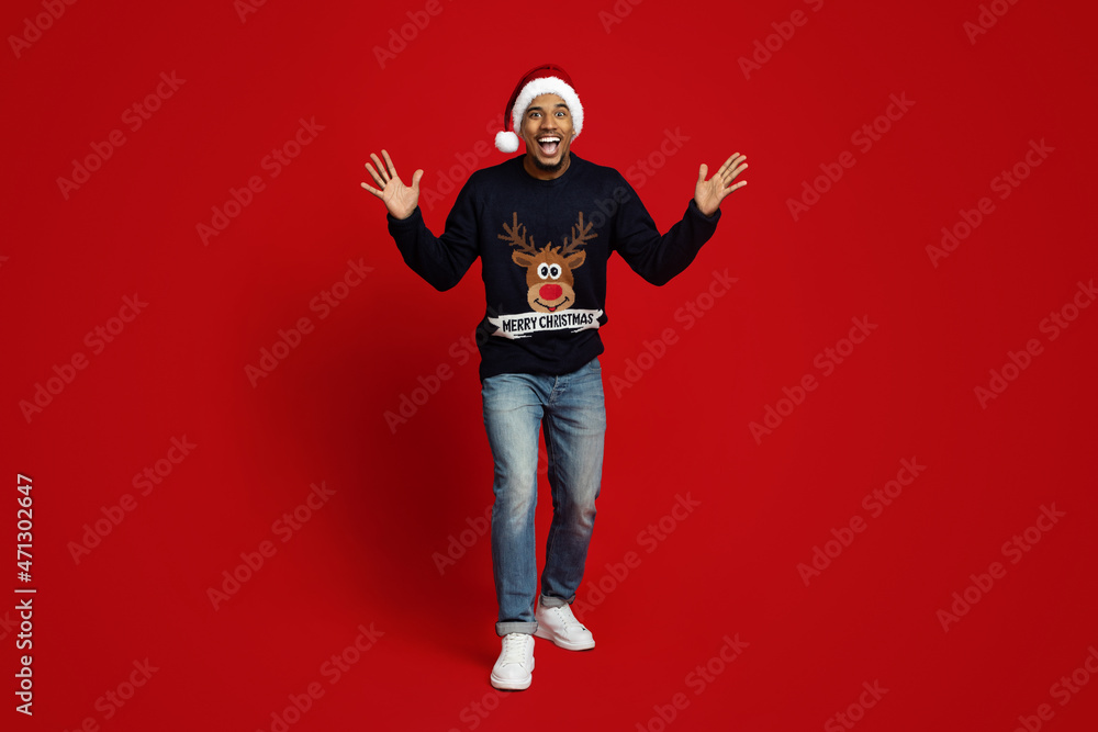 Surprised black guy in Santa hat gesturing on red background Surprised black guy in Santa hat gesturing on red background