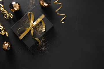Gold and black gift and baubles on a black background with Christmas decorations. View from above. Space for text.