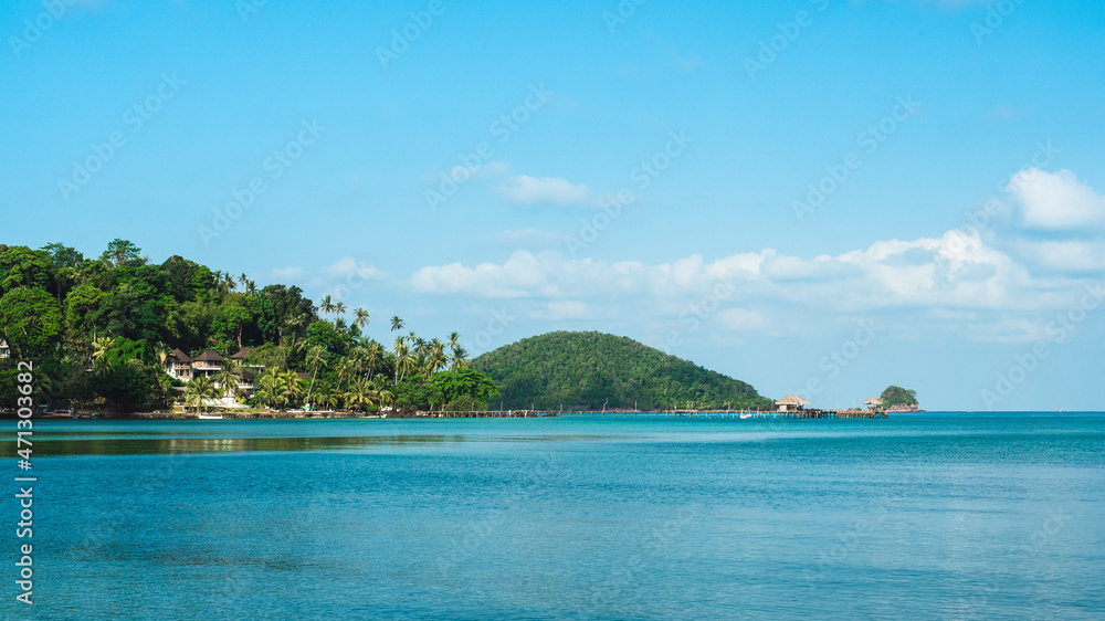 Scenic view of peaceful tropical island with long wooden pier landmark over turquoise sea water against blue sky. Koh Mak Island, Trat, Thailand.