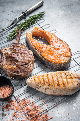 Set of bbq grilled meat steaks salmon, beef and turkey on a grill. Gray background. Top view