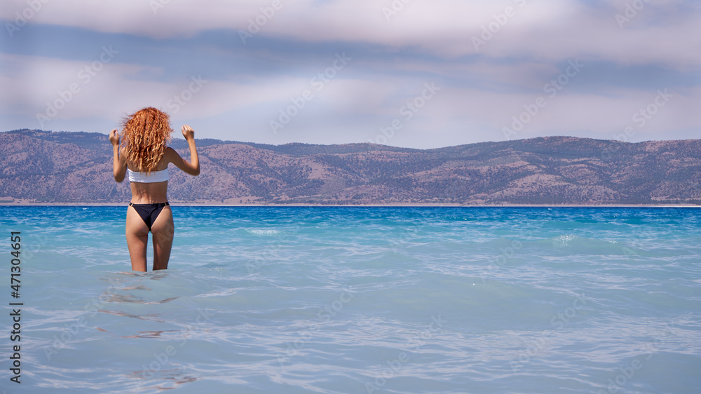Summer vacation style with beautiful slim red haired girl in  bikini walking on the white sand beach. Traveler women happy in the blue crystal clear sea in Salda crater lake - Burdur, Turkey.