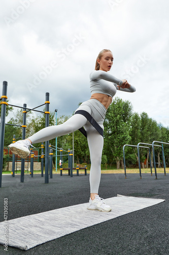 Resistance band fitness outdoors. Young athletic woman with perfect body in sportswear doing exercises with strap elastic in the city park