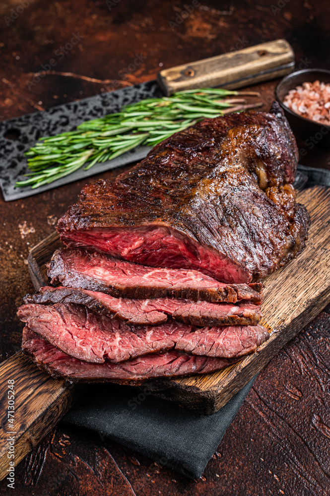 Roasted hanging tender or Onglet sliced beef meat steak on a butcher board with cleaver. Dark background. Top View