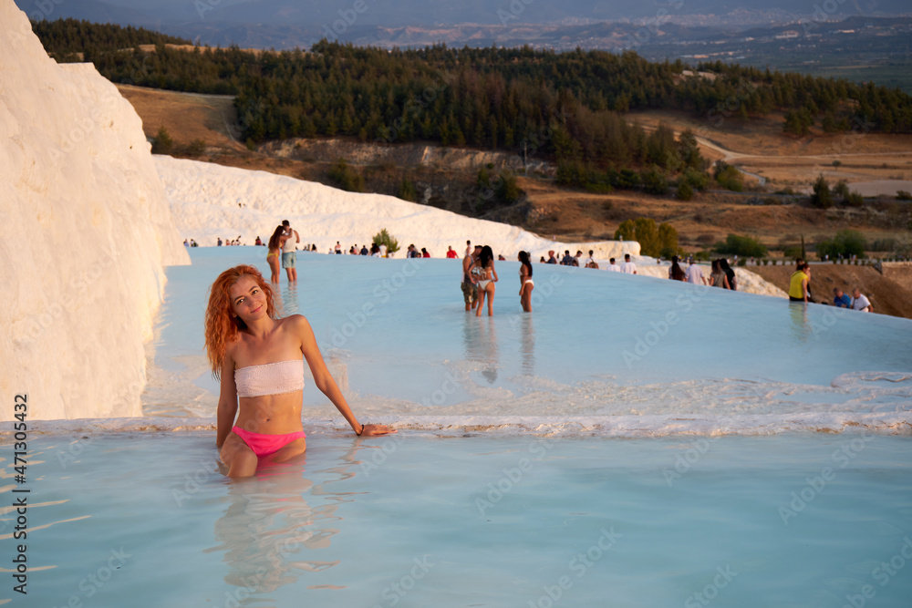 Pamukkale travertine in Turkey with woman enjoying the views. Red hair woman traveler swimming at Pamukkale Natural Park and looking at beautiful sunset.Sexy young woman rest in Pamukkale.