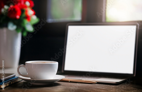 Focus on white coffee cup with computer laptop, mobile on book and vase with flower near window with sunlight shining through, Dark tone