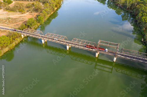 Aerial view of a truck crossing a metal span bridge over a wide green river photo