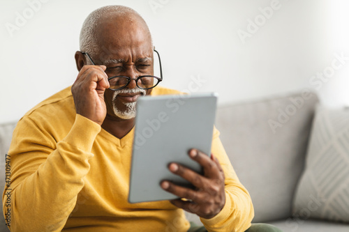 Senior Man With Poor Eyesight Using Tablet Squinting Eyes Indoor
