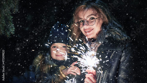 Mother and daughter holding burning sparkler outside and making a Christmas wish