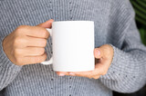 Woman in warm sweater holding white mug in hands. Winter cup Mockup for Christmas individual gifts design