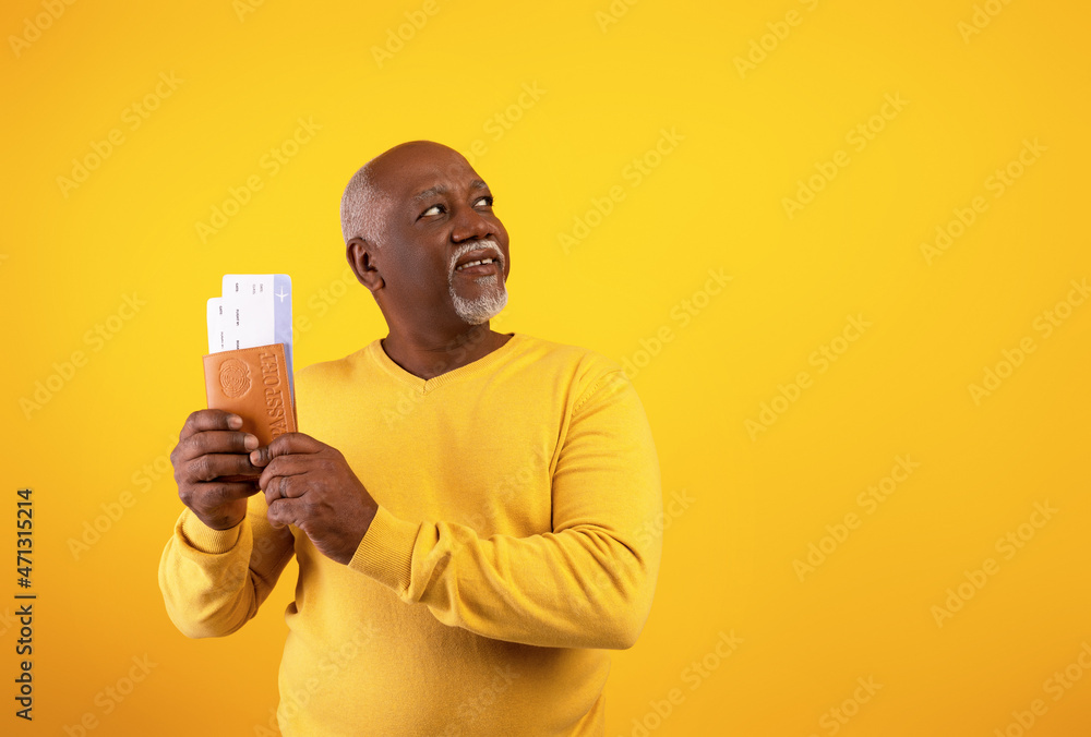 Happy senior black man holding passport with plane boarding tickets, looking aside at empty space on orange background Happy senior black man holding passport with plane boarding tickets, looking aside at empty space on orange background