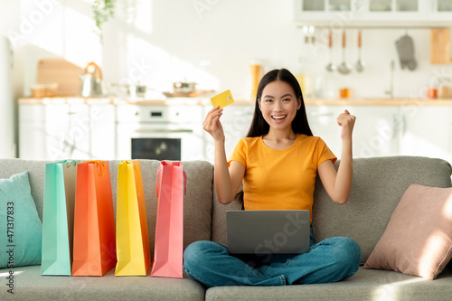 Excited asian lady with laptop computer and shopping bags purchasing via internet, holding credit card and smiling © Prostock-studio