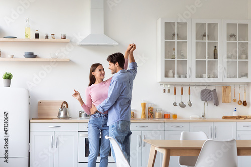 Cheerful millennial european husband and wife have fun and dancing in modern kitchen interior