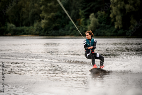 view of young woman in wetsuit riding on river water on wakeboard holding rope with her hands