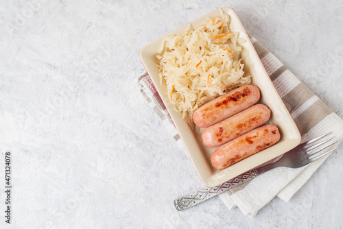 Top view of traditional dish is fried sausages and pickled cabbage salad in a red rectangular plate with fork on a napkin on light table