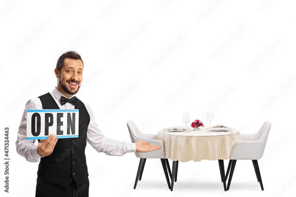 Waiter holding a sign open and gesturing welcome next to a restaurant table Waiter holding a sign open and gesturing welcome next to a restaurant table