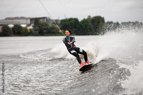 Young attractive woman in swimsuit riding splashes wave on wakeboard holding rope