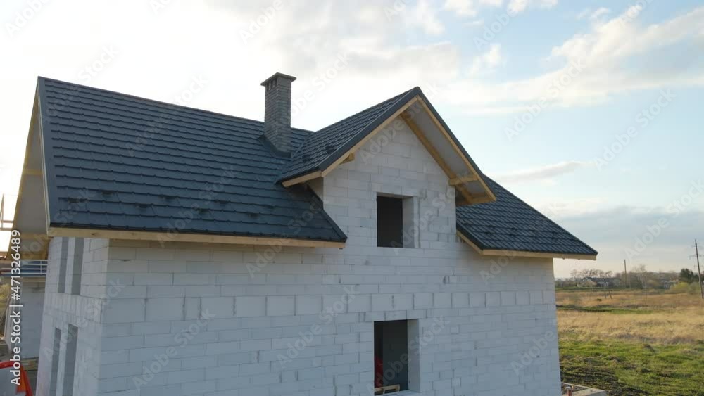 Aerial view of unfinished house with aerated lightweight concrete walls and wooden roof frame covered with metallic tiles under construction Aerial view of unfinished house with aerated lightweight concrete walls and wooden roof frame covered with metallic tiles under construction