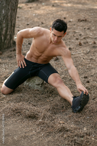 Full length image of a athletic sportsman doing stretching exercises in the park.