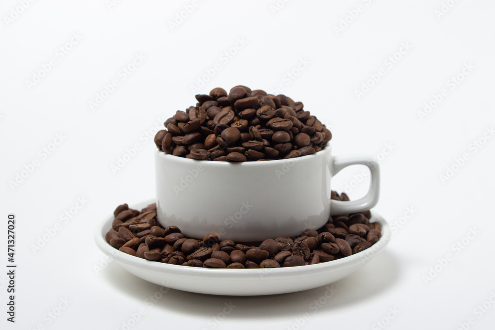 White cup overflowing with coffee beans on a white background. Freshly roasted coffee beans White cup overflowing with coffee beans on a white background. Freshly roasted coffee beans