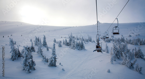Ski lift at the top in snowy mountains lifts person up the slope, path extending beyond the horizon
