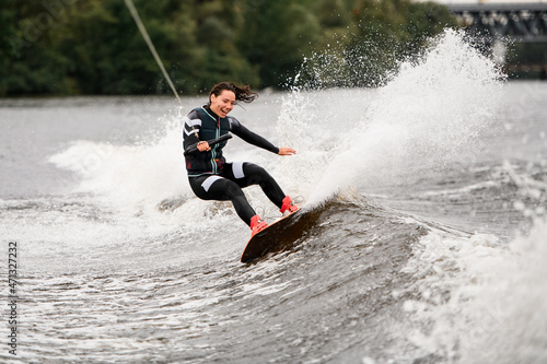 laughing woman balances on splashing wave on wakeboarding board holding rope with her han
