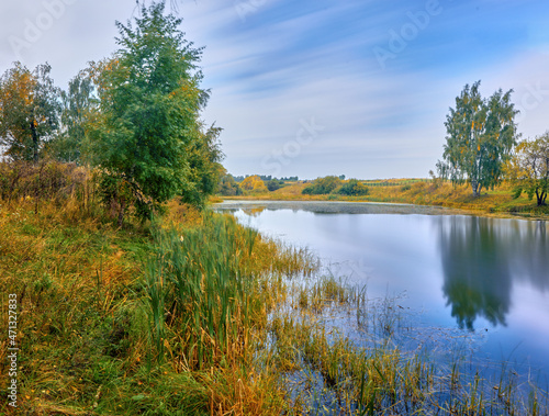 Bright multicolored autumn trees with golden foliage on the riverbank and reflected on a clear day. Russia, the Volga river.