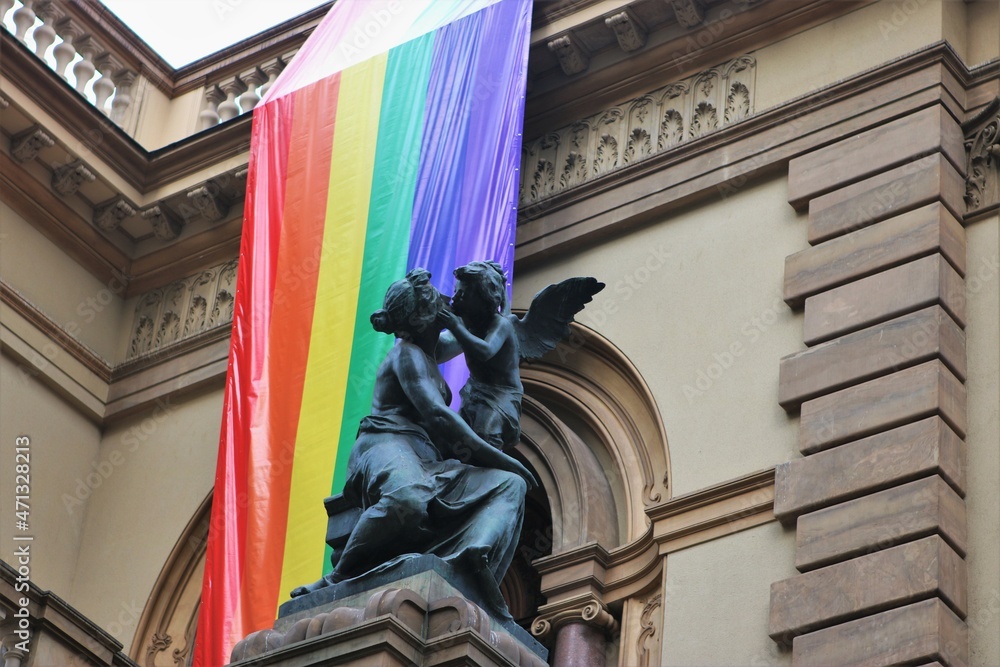 Fototapeta premium LGBT pride flag hanging from the Theatro Municipal de São Paulo behind a statue of a kissing angel