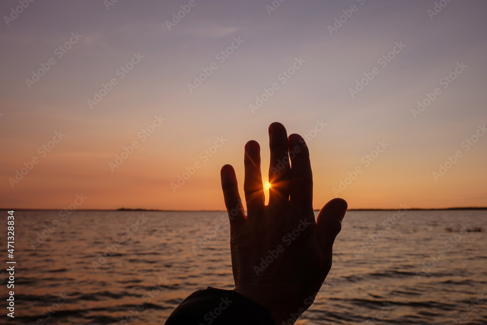 Female hand at sunset. The happy woman passes the sun's rays through her fingers.