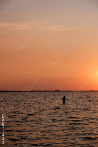 Fototapeta Naklejka Na Ścianę i Meble -  Silhouette of a lonely man in the water on a coral color sunset background. Svityaz lake sunset. Vertical image. 