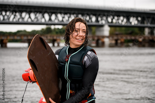 young wet and cheerful woman standing with board for wakeboarding in her hand photo