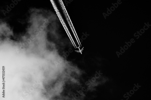 Photography Airplane leaves contrails in the sky with clouds on black background