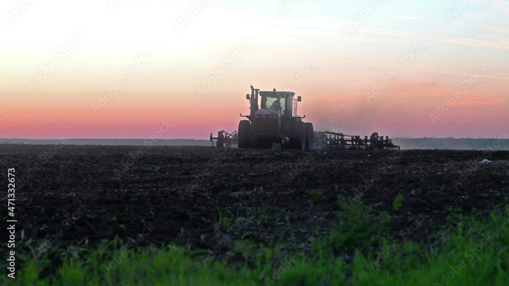 processing the field with a red tractor, cultivation before planting plants at sunset processing the field with a red tractor, cultivation before planting plants at sunset
