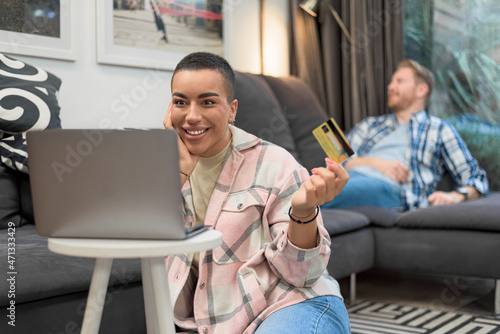 Holiday shopping online young african american woman purchasing web shop, entrepreneur pays using laptop, happy mixed races girl is enjoying buying gifts and sitting on floor with her laptop at home. photo