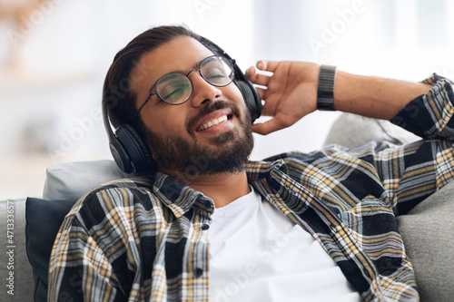Closeup of joyful indian guy listening to music  using headset