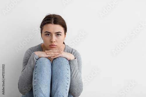 Scared sad worried millennial european woman sits on floor at home interior, on gray wall background