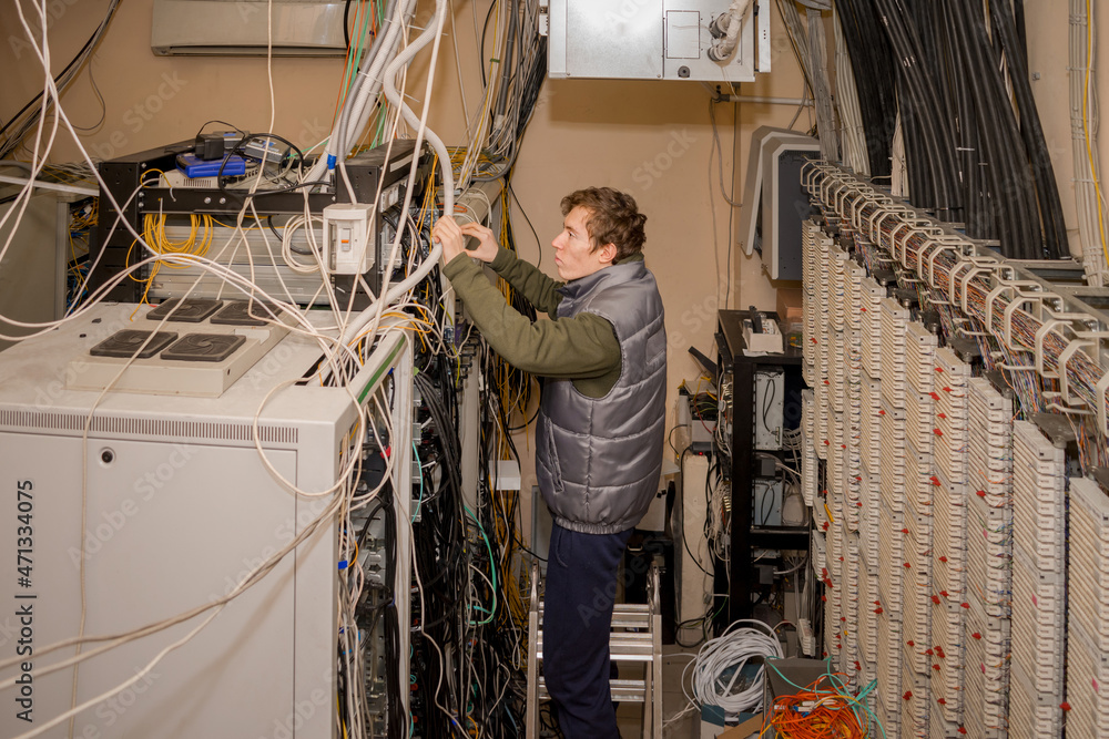 A technician is standing on the stairs and laying wires in the server room.  Maintenance of computer equipment in the old data center. The man works  near the server racks. Stock-Foto