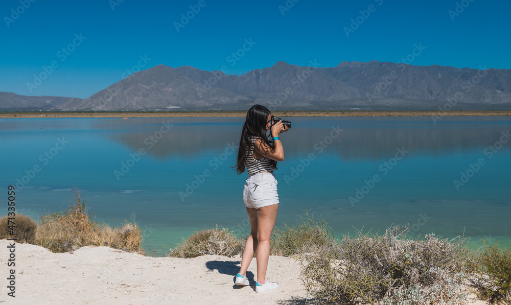 Fotka „Girl explorer photographing the "Playitas" lagoon in Cuatrociénegas,  Coahuila, Mexico. Dressed in white shorts for the desert heat, she takes  pictures and enjoys the oasis landscape “ ze služby Stock