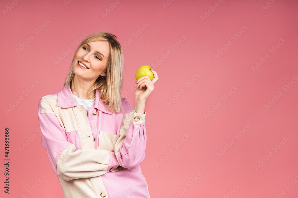 Healthy eating diet concept. Portrait of cheerful young blonde woman holding and eating green apple isolated on pink background. Healthy eating diet concept. Portrait of cheerful young blonde woman holding and eating green apple isolated on pink background.