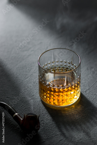 Glass with whiskey and tube in a strip of light on a dark background 
